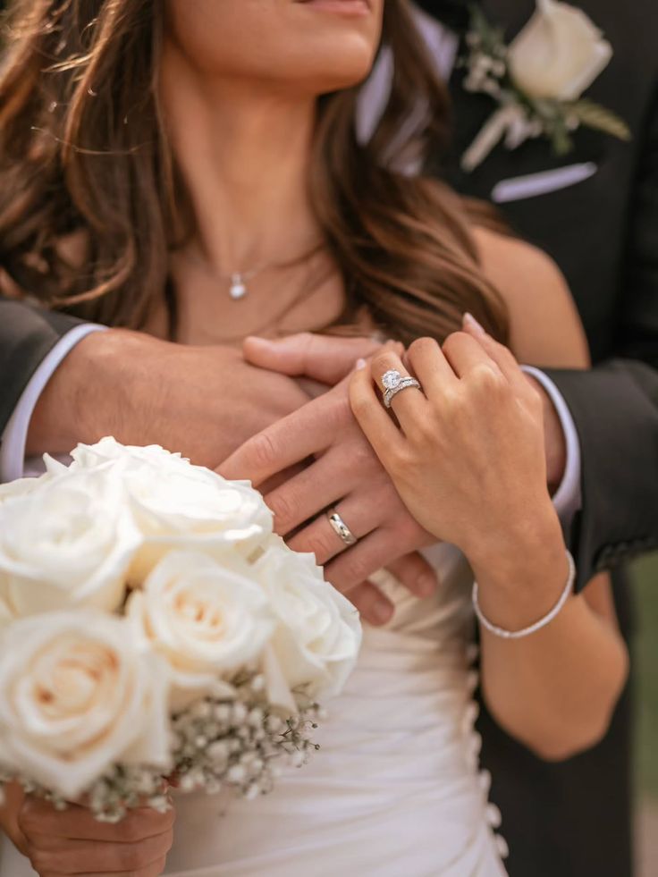 Joined hands with wedding rings and white roses